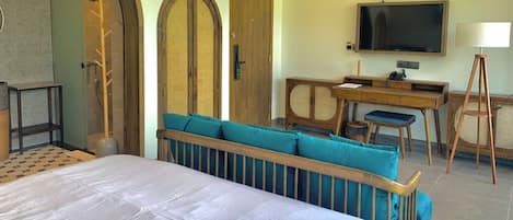Una habitación de hotel con cama, zona de estar con cojines, escritorio con silla, televisor y ventana.