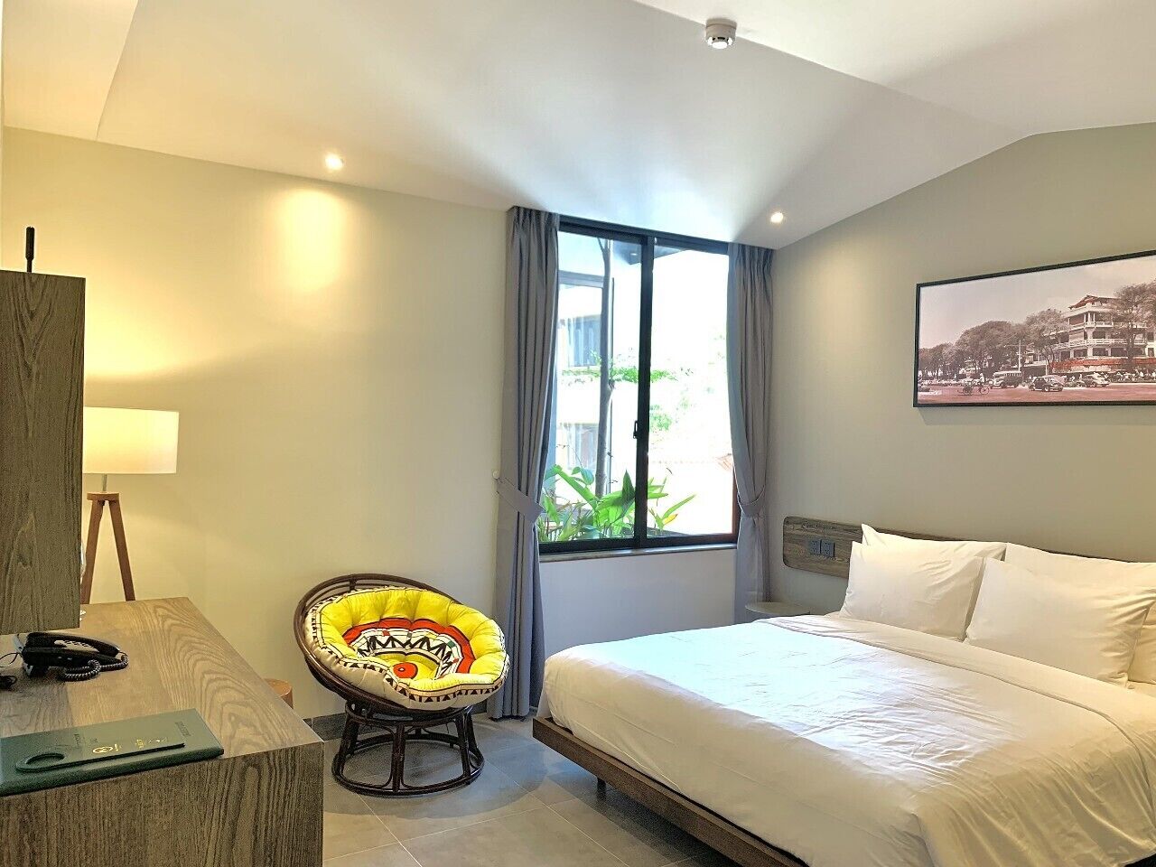 A hotel room with a bed, a desk with a lamp, a chair, and a window with curtains.