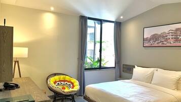 A hotel room with a bed, a desk with a lamp, a chair, and a window with curtains.