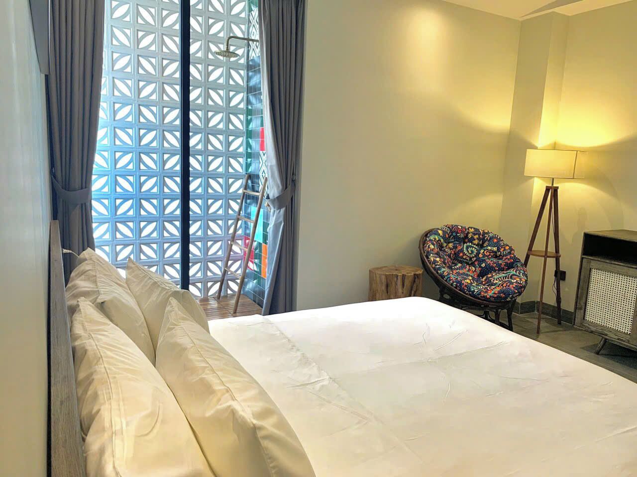 Ein Hotelzimmer mit einem Bett, einem Sessel, einer Lampe und einem fenster mit Vorhängen.