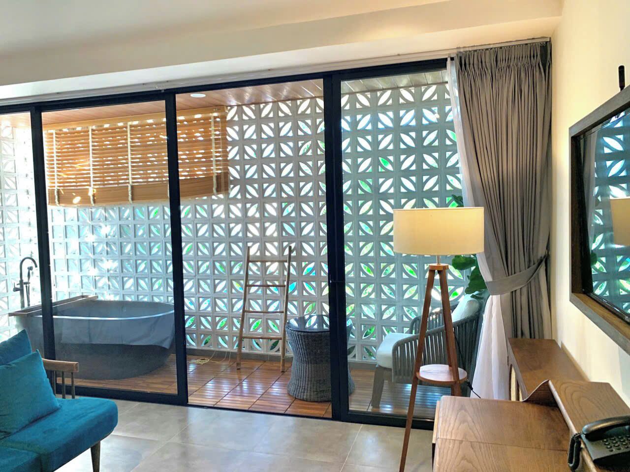 A modern room with a sliding glass door leading to a balcony, a bathtub, a wooden ladder, and a small table with a lamp.