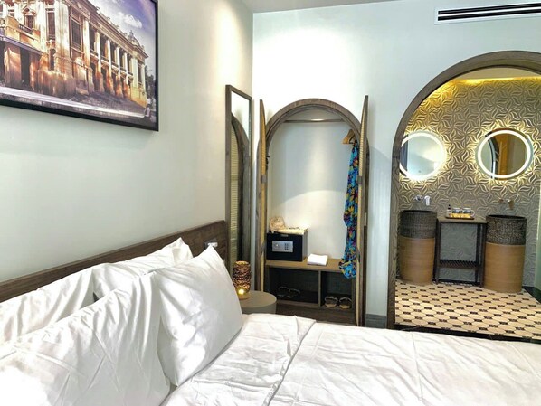A hotel room with a bed, a mirror, a vanity with a sink, and a patterned wall. - The Mystery Con Dao (Ho Chi Minh City)