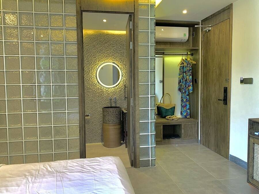 A modern hotel room with a bed, a vanity with a mirror, and a bathroom visible through an open door.