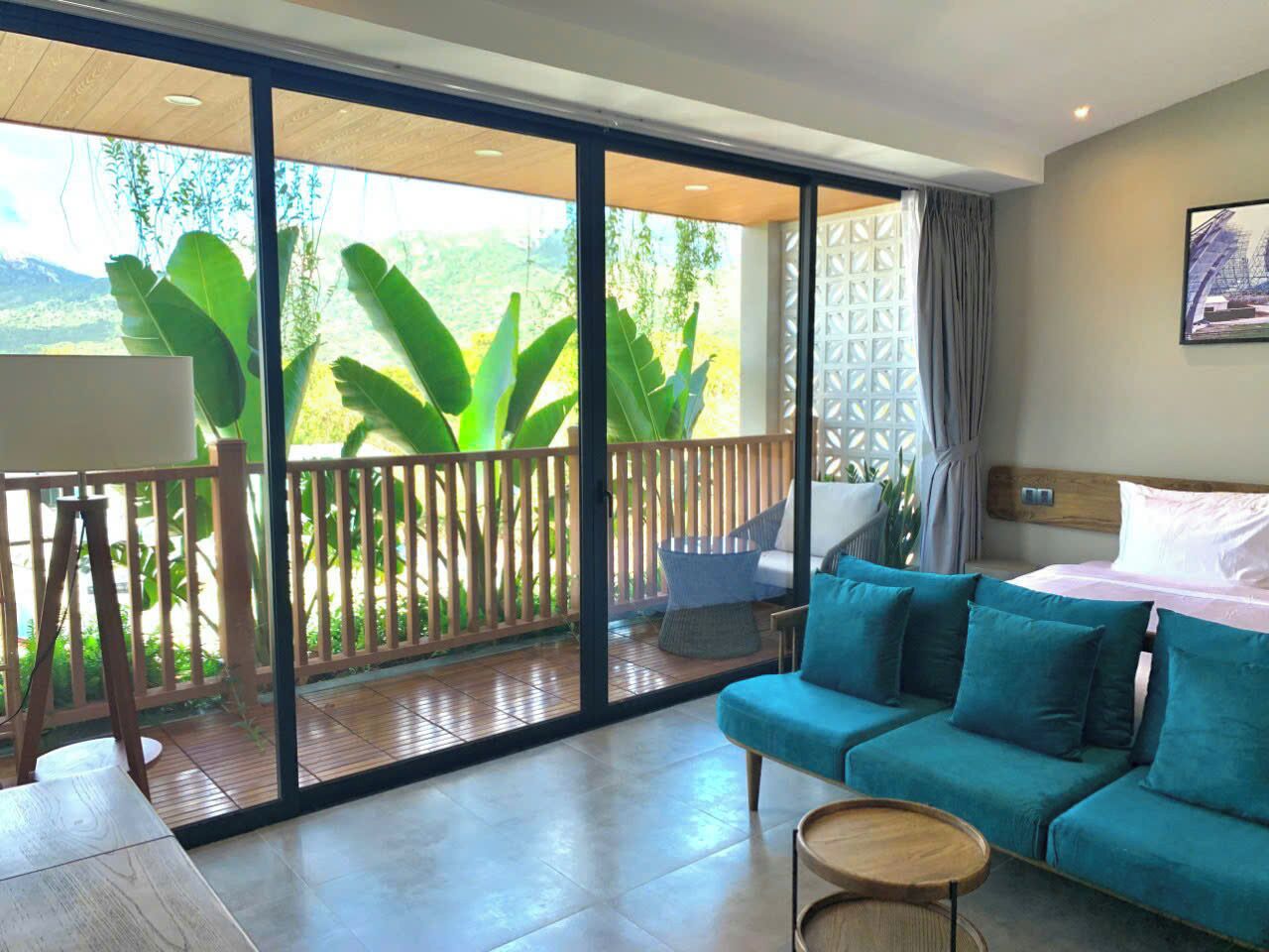 Una habitación con sofá, una mesita, cama y balcón con vistas al verdor.