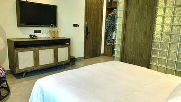 Een slaapkamer met een groot bed, een aan de muur bevestigde televisie, een houten kast met rieten manden en een inloopkast met glazen deur.