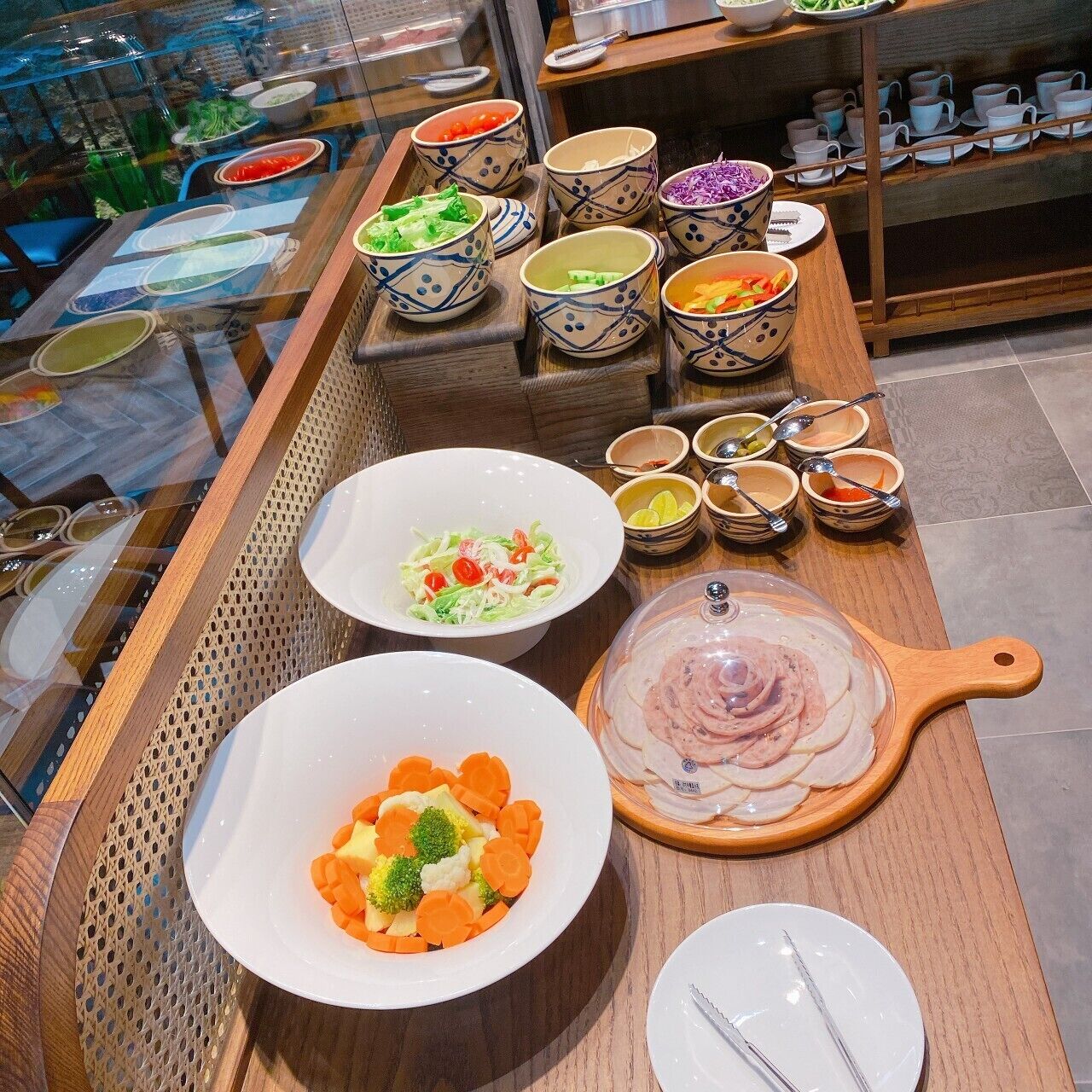 A buffet table with various dishes, including bowls of salad, sliced meat, and bowls of soup.