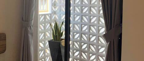 A sliding glass door leading to a balcony with a geometric white lattice partition, a potted plant, and a wooden floor.