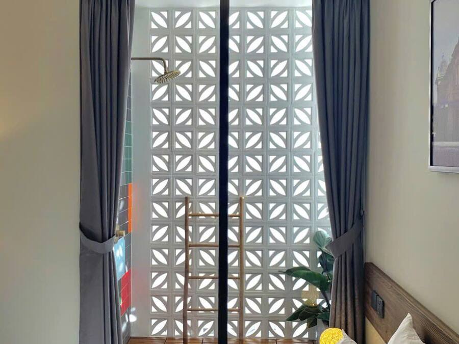A hotel room with a bed, a small round table with a lamp, a wooden floor, and a view through a window with a lattice screen.