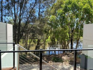 A modern building with a glass balcony overlooking a natural landscape with trees and a body of water. - Lovely Water Front Family Home in Robina QLD (Robina)