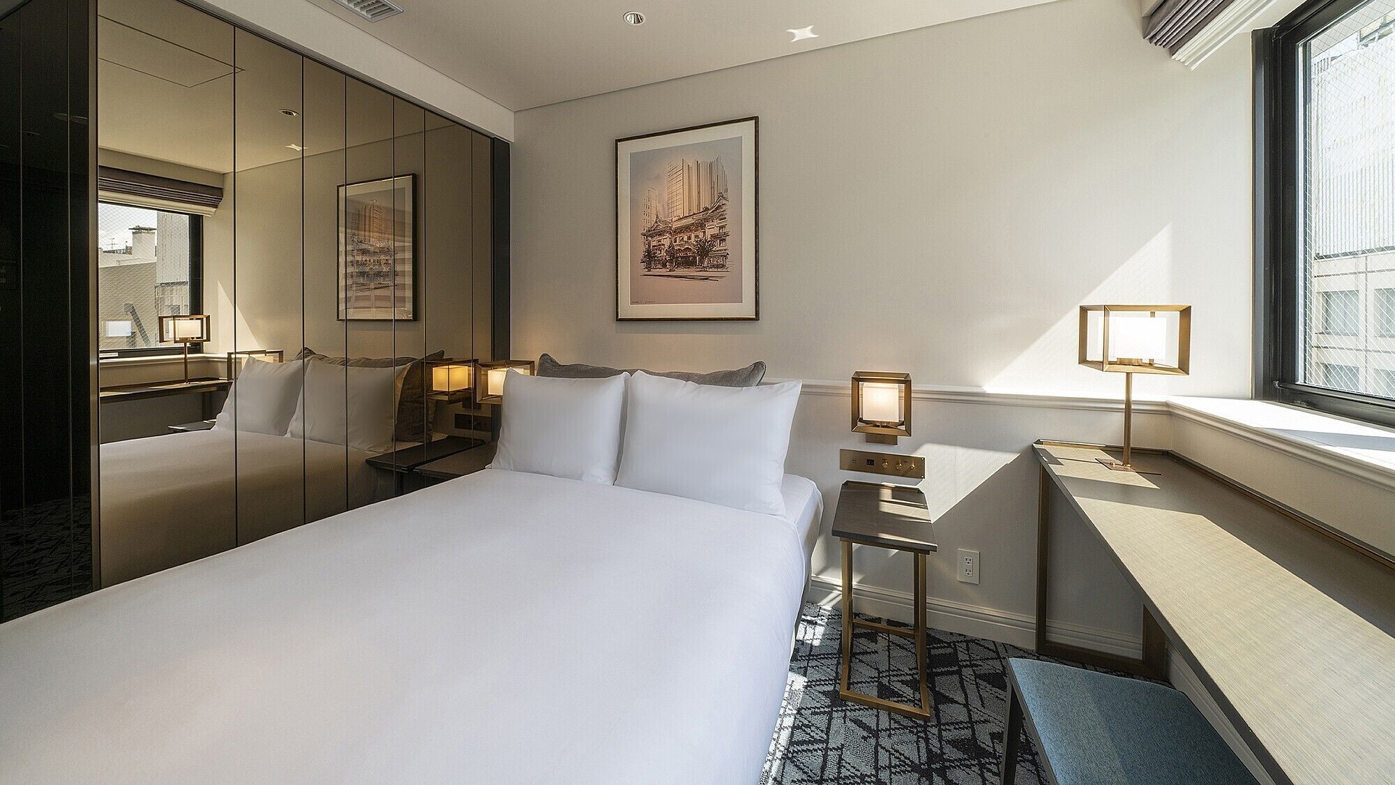 Quarto de hotel com uma cama grande, uma escrivaninha, uma cadeira, um espelho e uma janela.