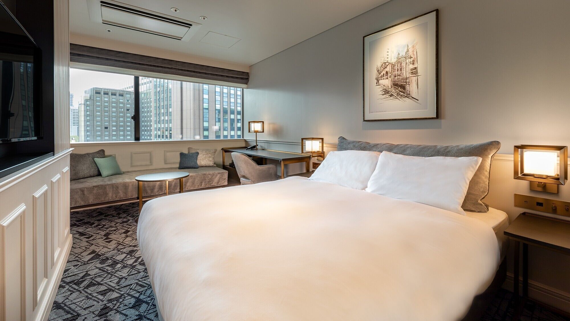 Quarto de hotel com uma cama grande, uma escrivaninha, um sofá e uma janela com vista para a cidade.