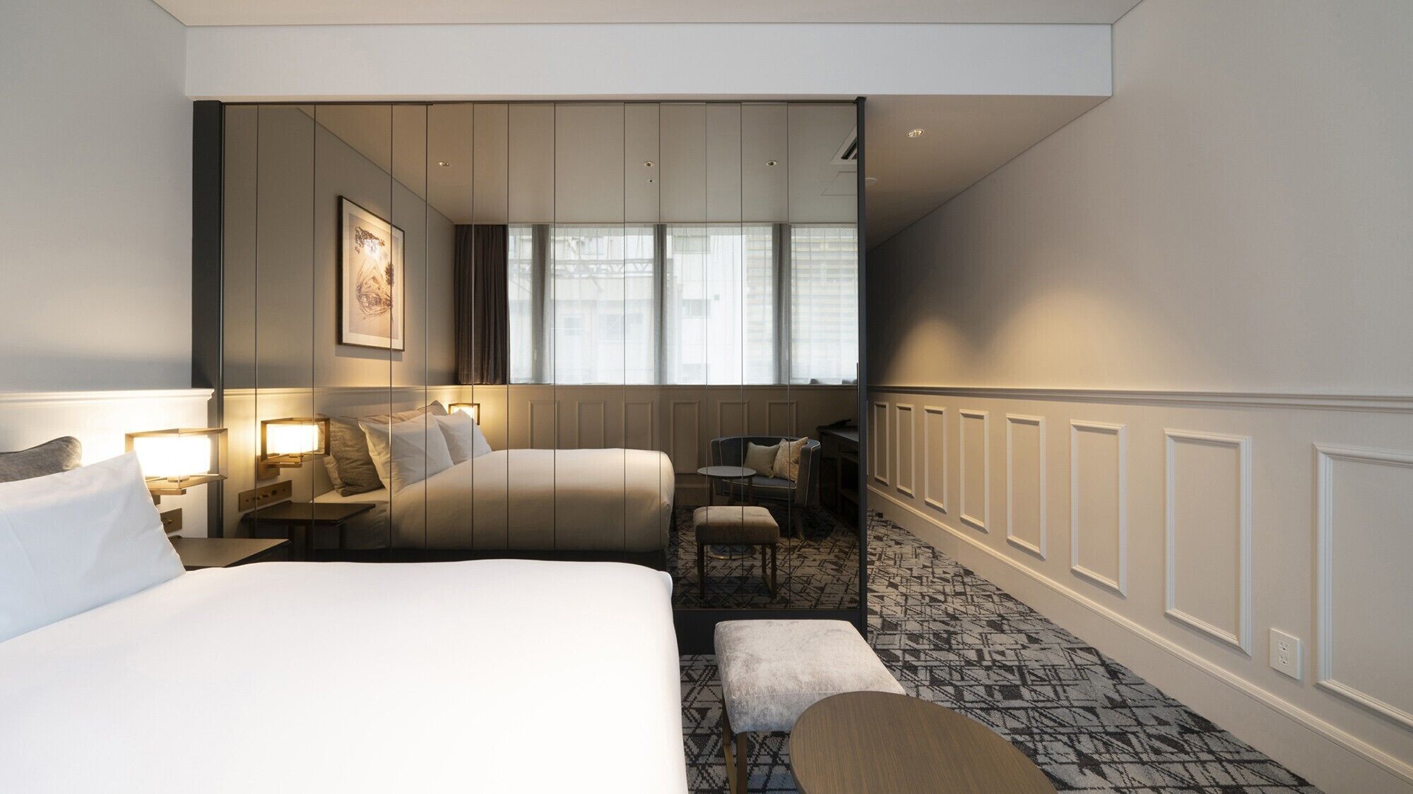 A hotel room with two beds, a desk, a chair, a small table, and a patterned carpet.
