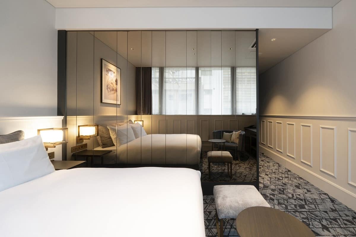 Hotellihuone, jossa on kaksi sänkyä, työpöytä, tuoli, pieni pöytä ja kuviollinen matto.