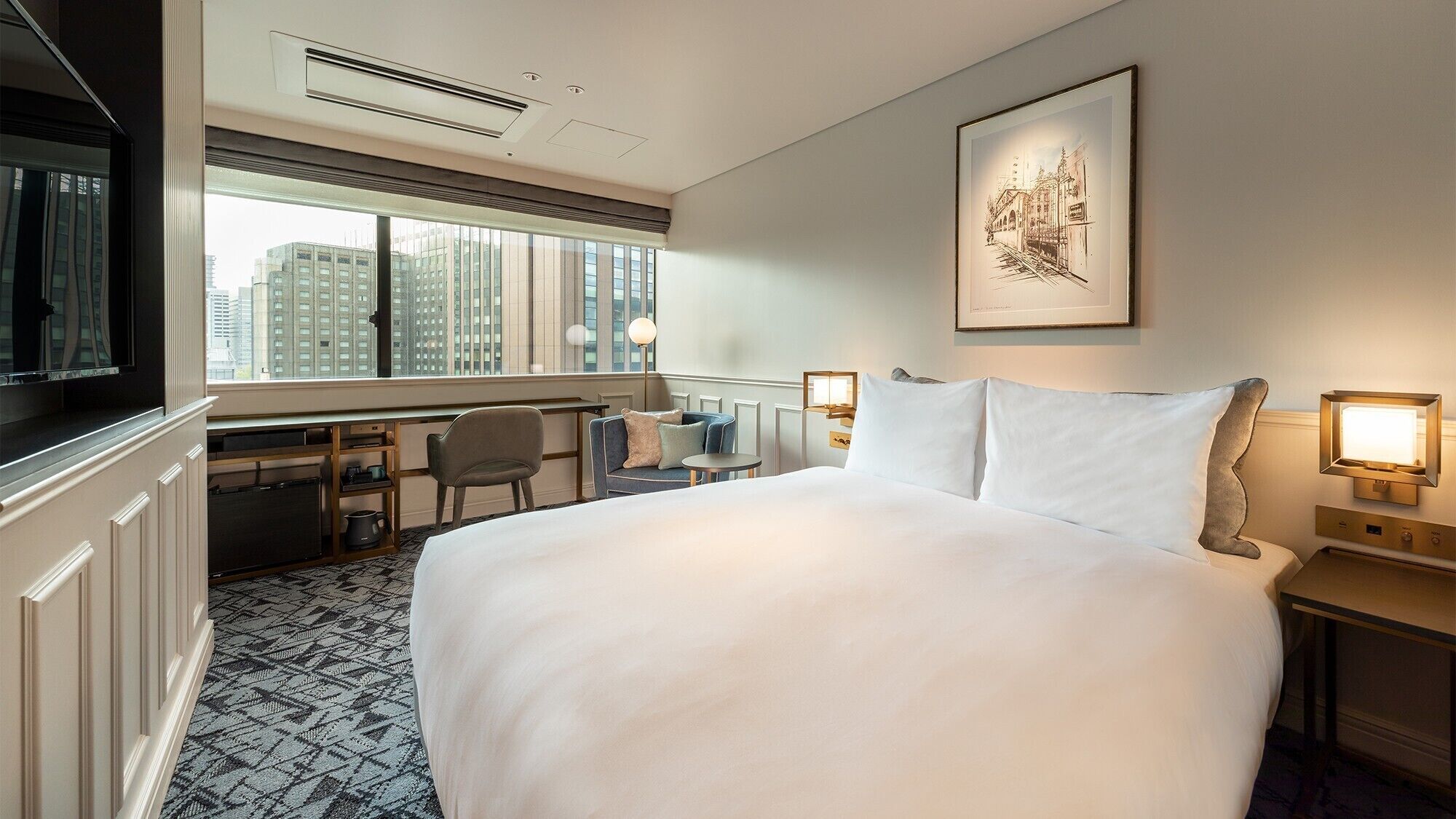 Quarto de hotel com uma cama grande, uma escrivaninha, uma cadeira, uma televisão e uma janela com vista para a cidade.