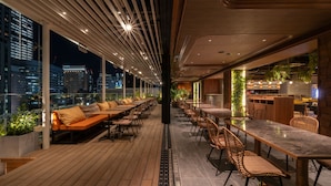 Um bar no terraço com piso de madeira, assentos e vista do horizonte urbano à noite.