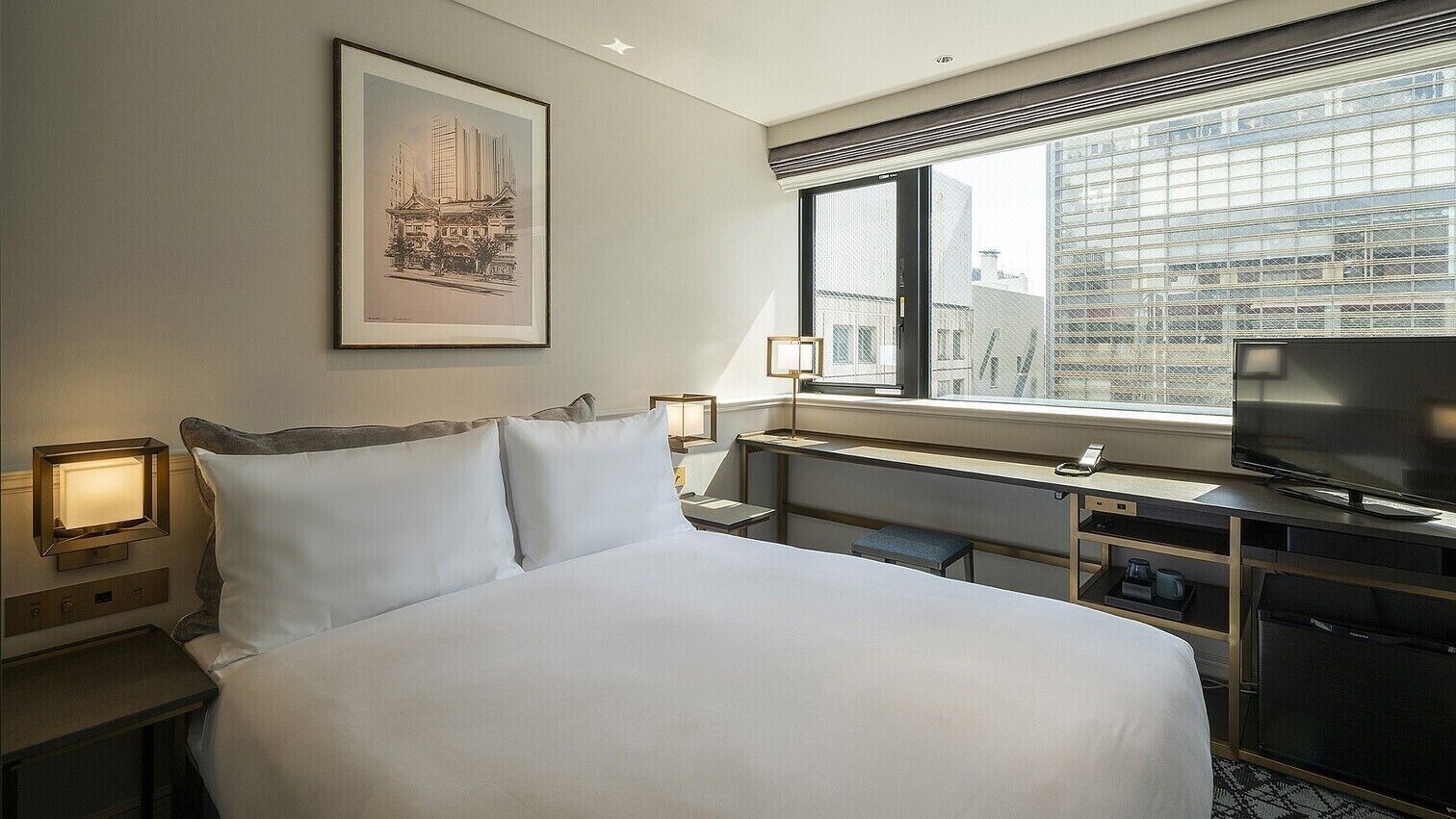 A hotel room with a bed, bedside tables, a desk with a television, and a window with a city view.