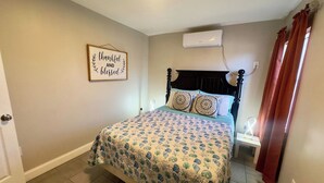 Ein Schlafzimmer mit einem Bett, einem Nachttisch, einer Wand-Klimaanlage und einem dekorativen Schild.