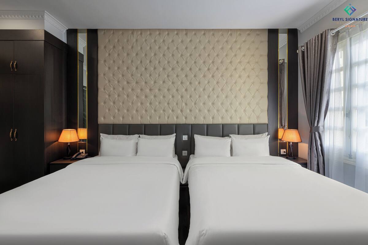 Une chambre d’hôtel avec un grand lit, deux tables de chevet, une tête de lit et des rideaux.