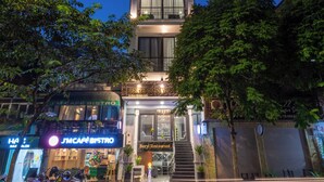 A modern hotel with a prominent tower structure, a ground-level restaurant, and a visible street with passing vehicles. - Beryl Signature Hanoi Hotel (Hanoi)
