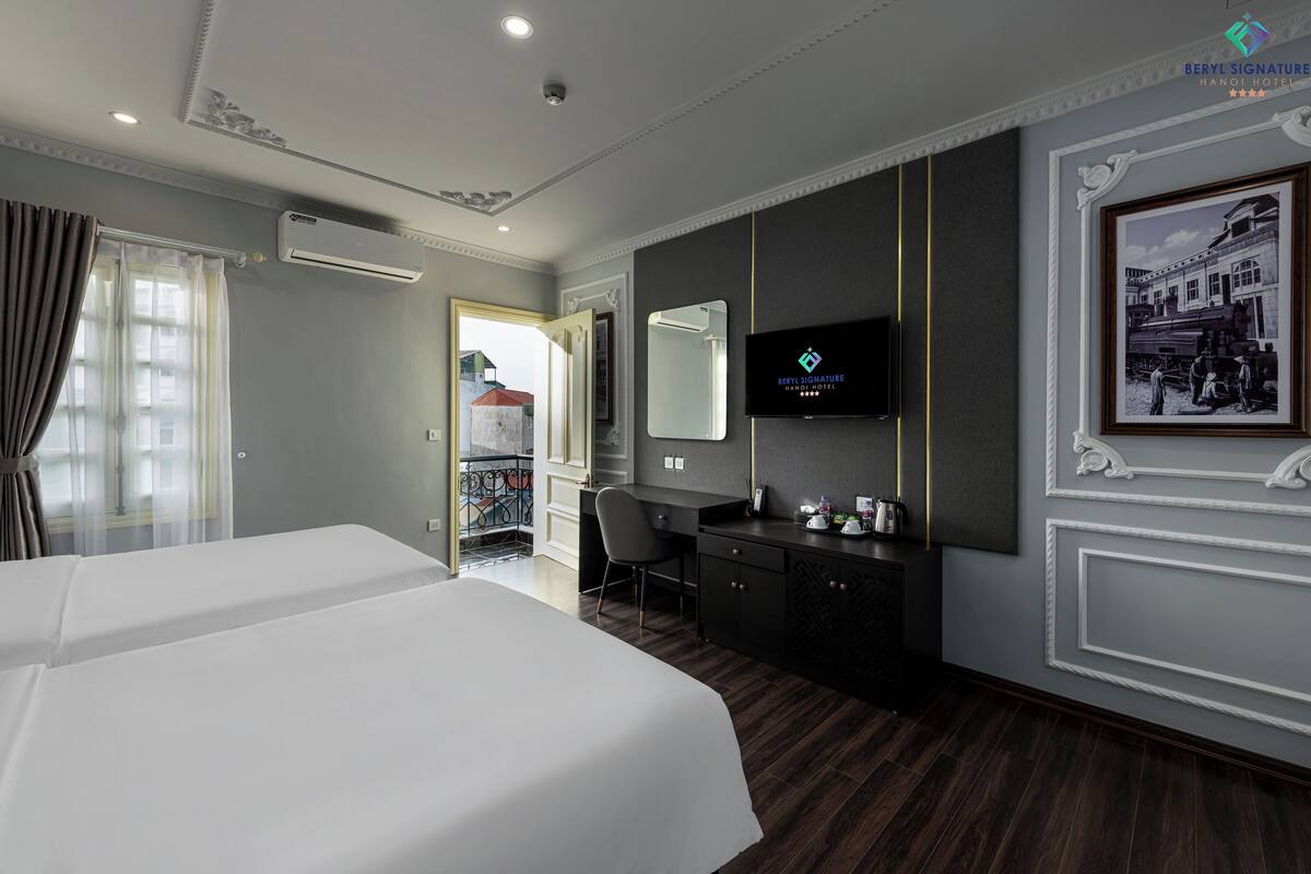 Une chambre d’hôtel avec deux lits, un bureau, une télévision et une grande fenêtre avec des rideaux.