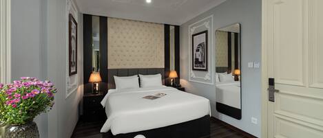 A hotel room with a large bed, bedside lamps, a mirror, and a vase of flowers.