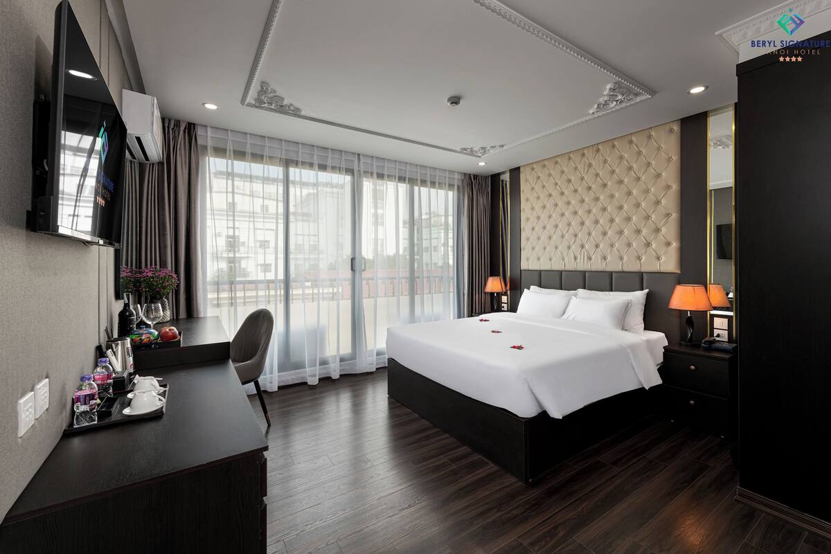 Une chambre d’hôtel avec un grand lit, un bureau avec une chaise, une télévision et une fenêtre avec des rideaux.