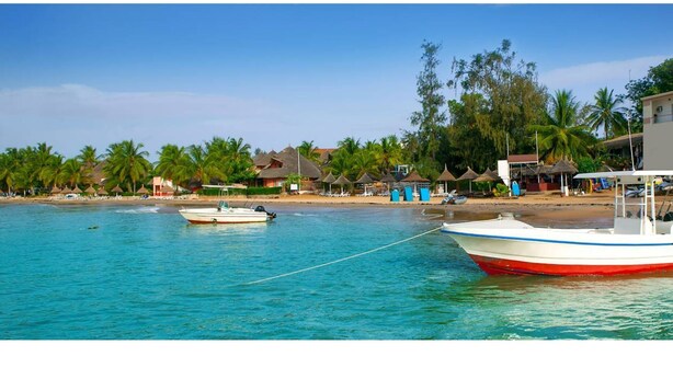 Une plage avec un bateau amarré au rivage, des palmiers et des cabanes de plage.