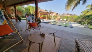 Une terrasse extérieure avec une piscine, un espace salon et des plantes tropicales.