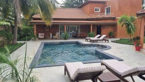 Une piscine avec des chaises longues, un espace patio et une maison avec un toit en tuiles.