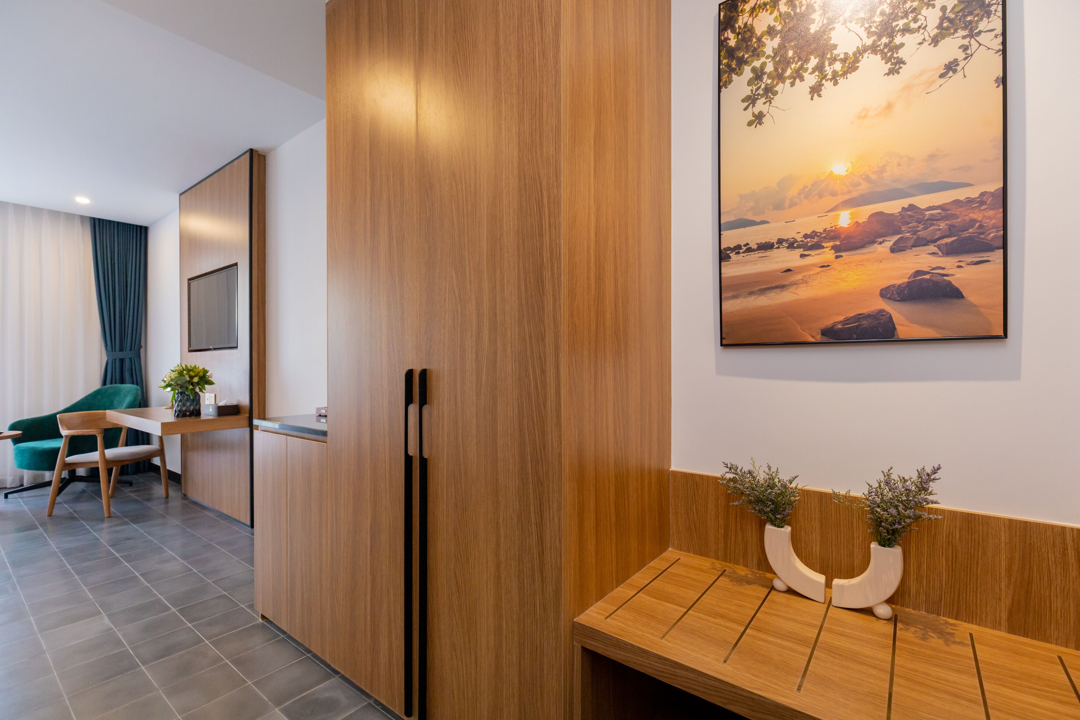 A modern hotel room with a wooden cabinet, a wooden bench, and a framed sunset painting.