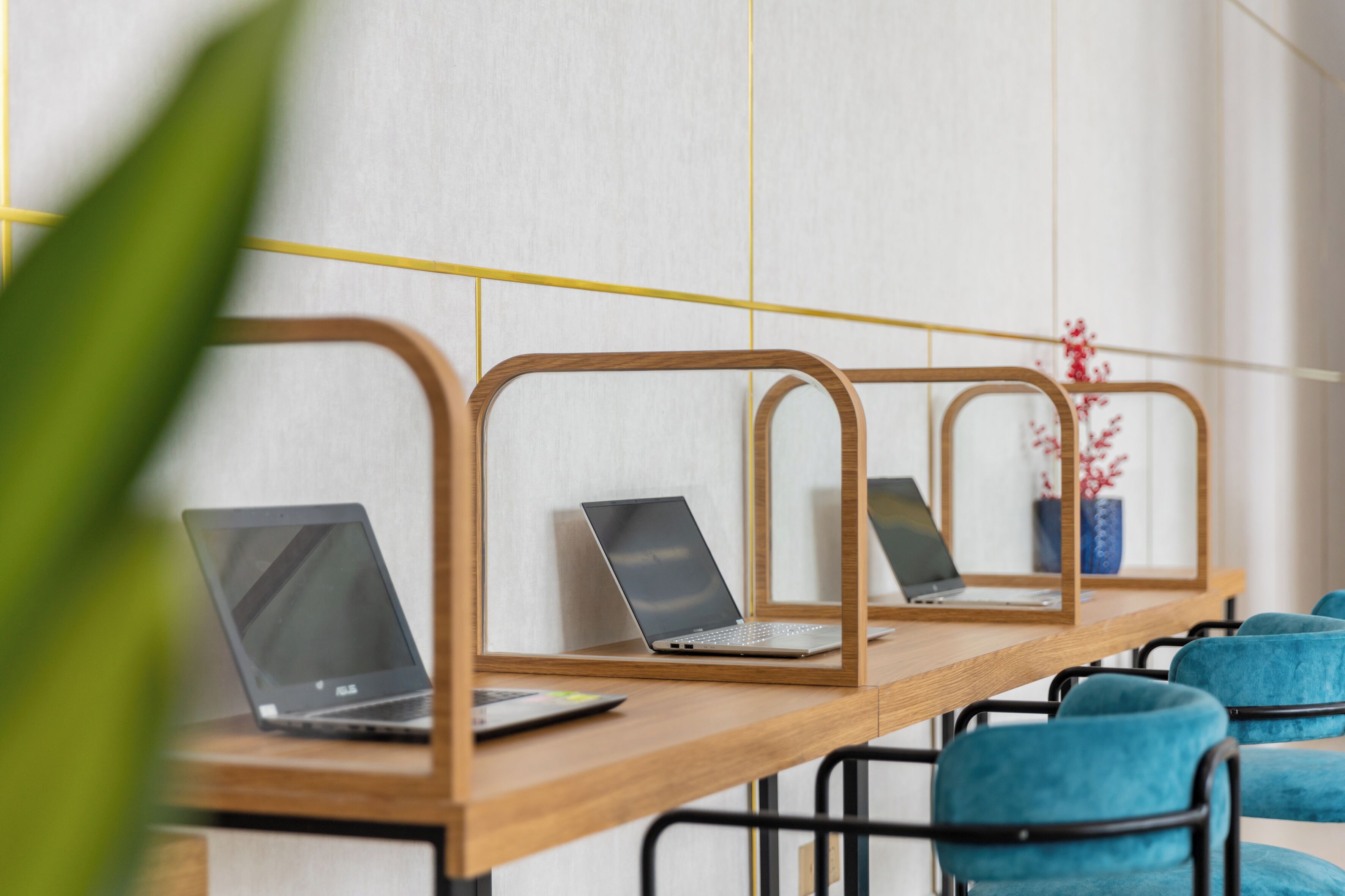 A long wooden table with three laptops and a vase with red flowers.