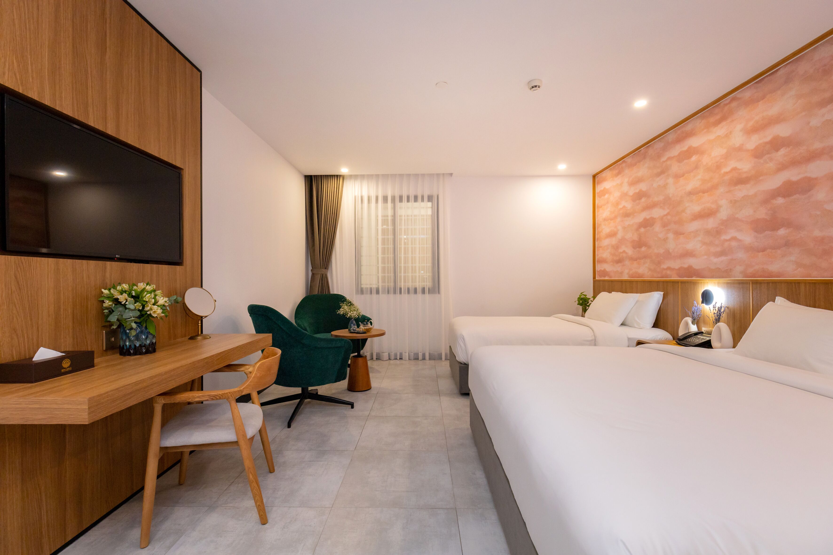 A modern hotel room with a wooden desk, a green chair, a bed with white linens, and a large wall-mounted TV.