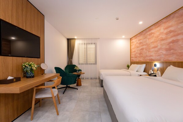 A modern hotel room with a wooden desk, a green chair, a bed with white linens, and a large wall-mounted TV.