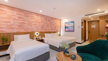 A modern hotel room with two beds, a wooden headboard, a round wooden table, and a teal armchair.