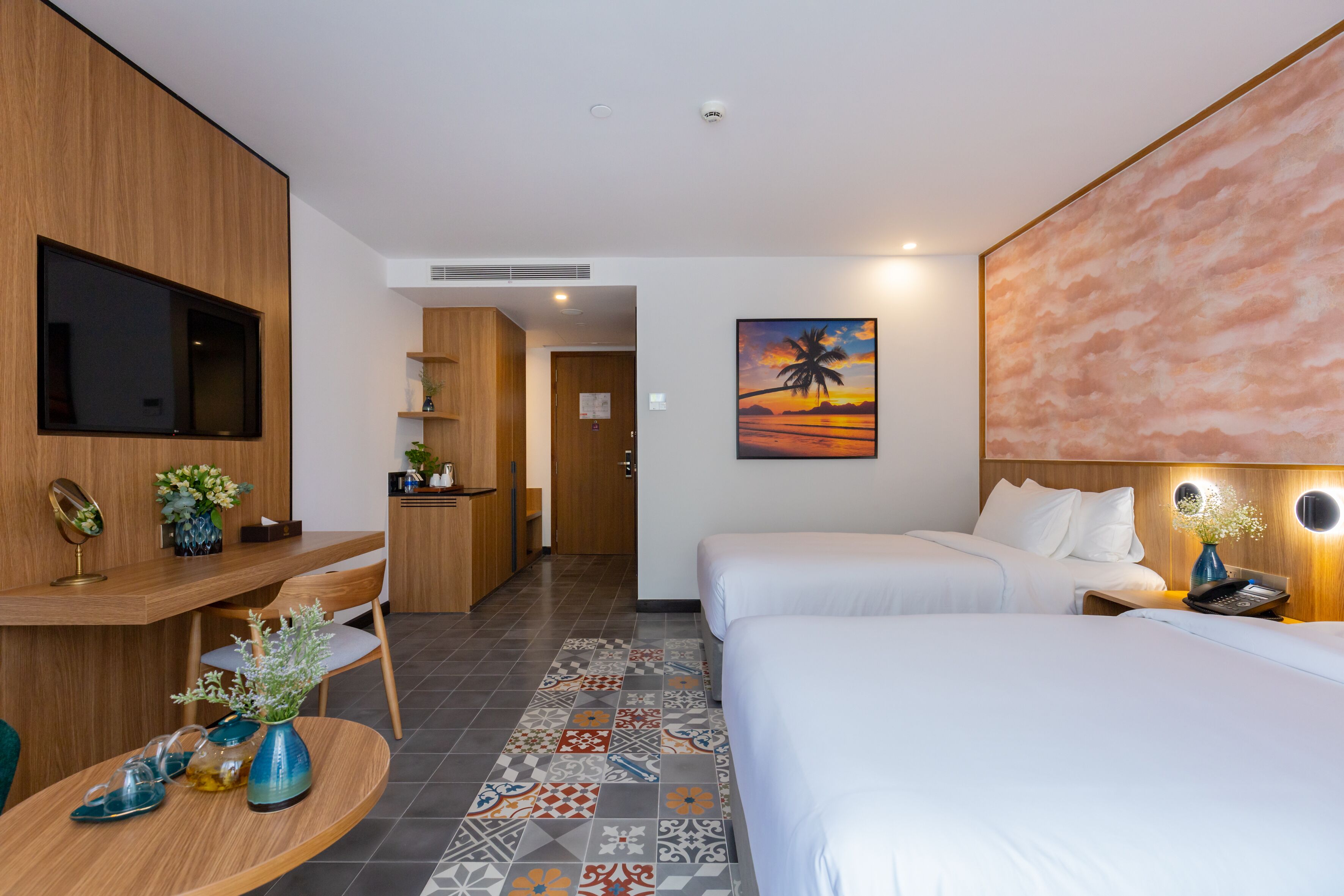 A hotel room with a bed, a desk, a chair, a TV, and a painting of a sunset.