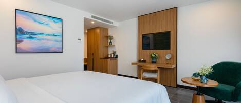A hotel room with a large bed, a desk with a chair, a small table with a vase, and a painting on the wall.