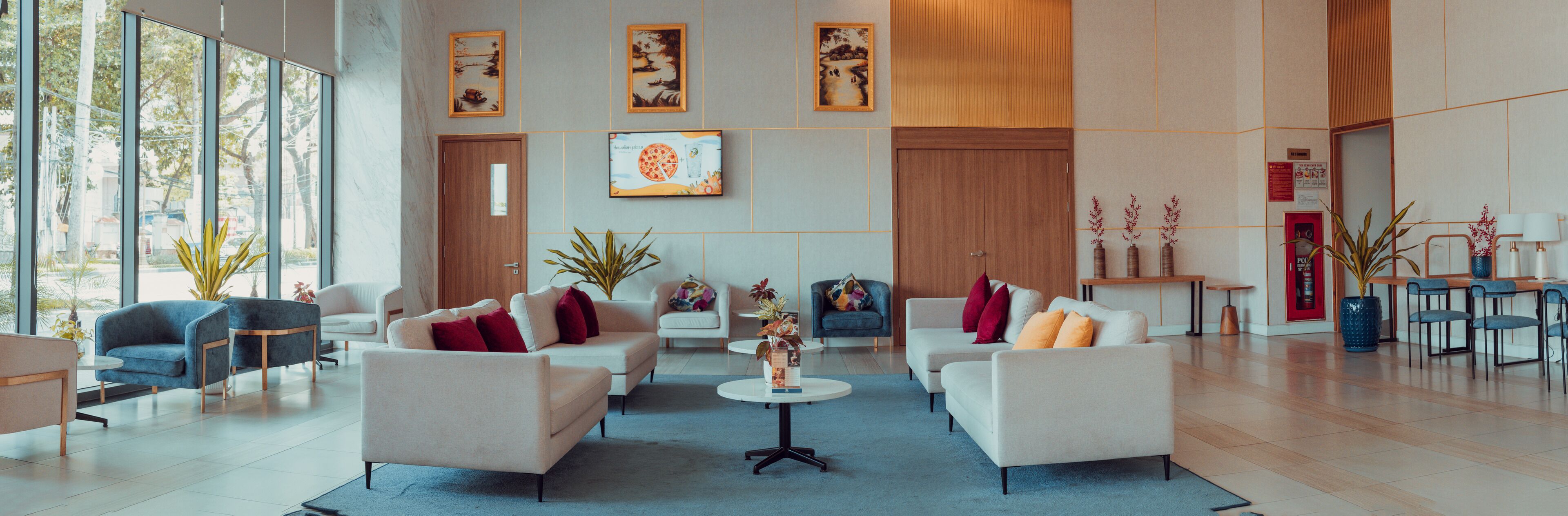 A spacious lobby with a modern design, featuring a seating area with sofas and armchairs, a coffee table, and a dining area with a table and chairs.