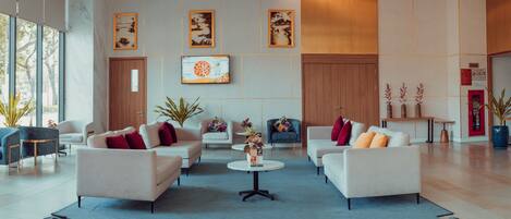 A spacious lobby with a modern design, featuring a seating area with sofas and armchairs, a coffee table, and a dining area with a table and chairs.
