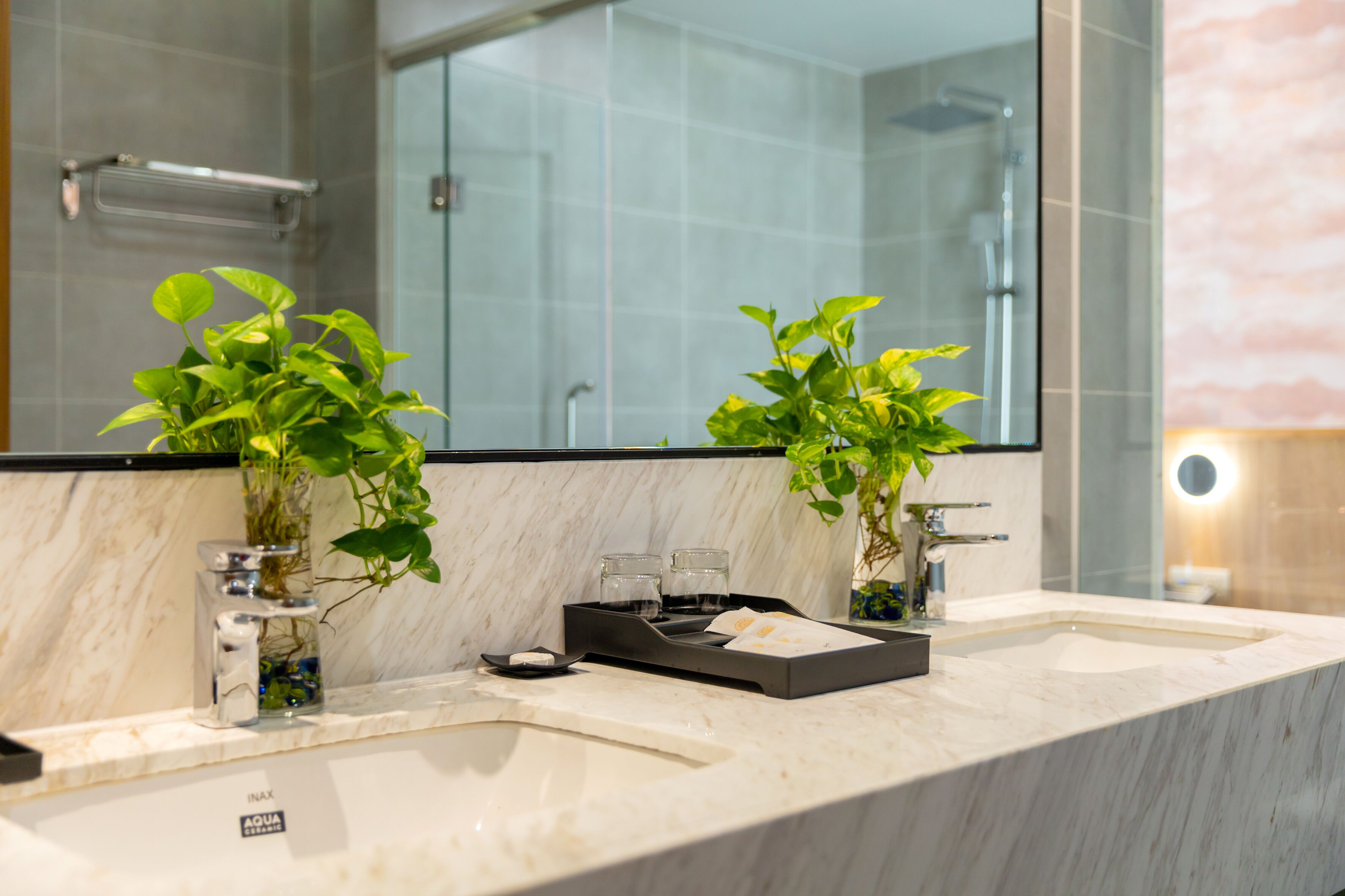 A bathroom with two sinks, a large mirror, and two potted plants.