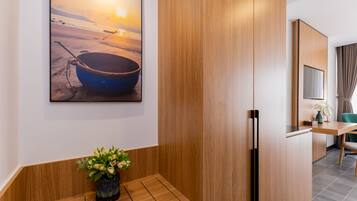 A modern hotel room with a wooden bench, a painting of a boat on a beach, and a wooden cabinet.