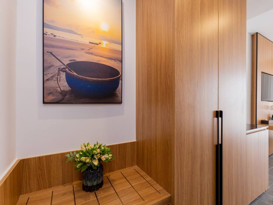A modern hotel room with a wooden bench, a painting of a boat on a beach, and a wooden cabinet.
