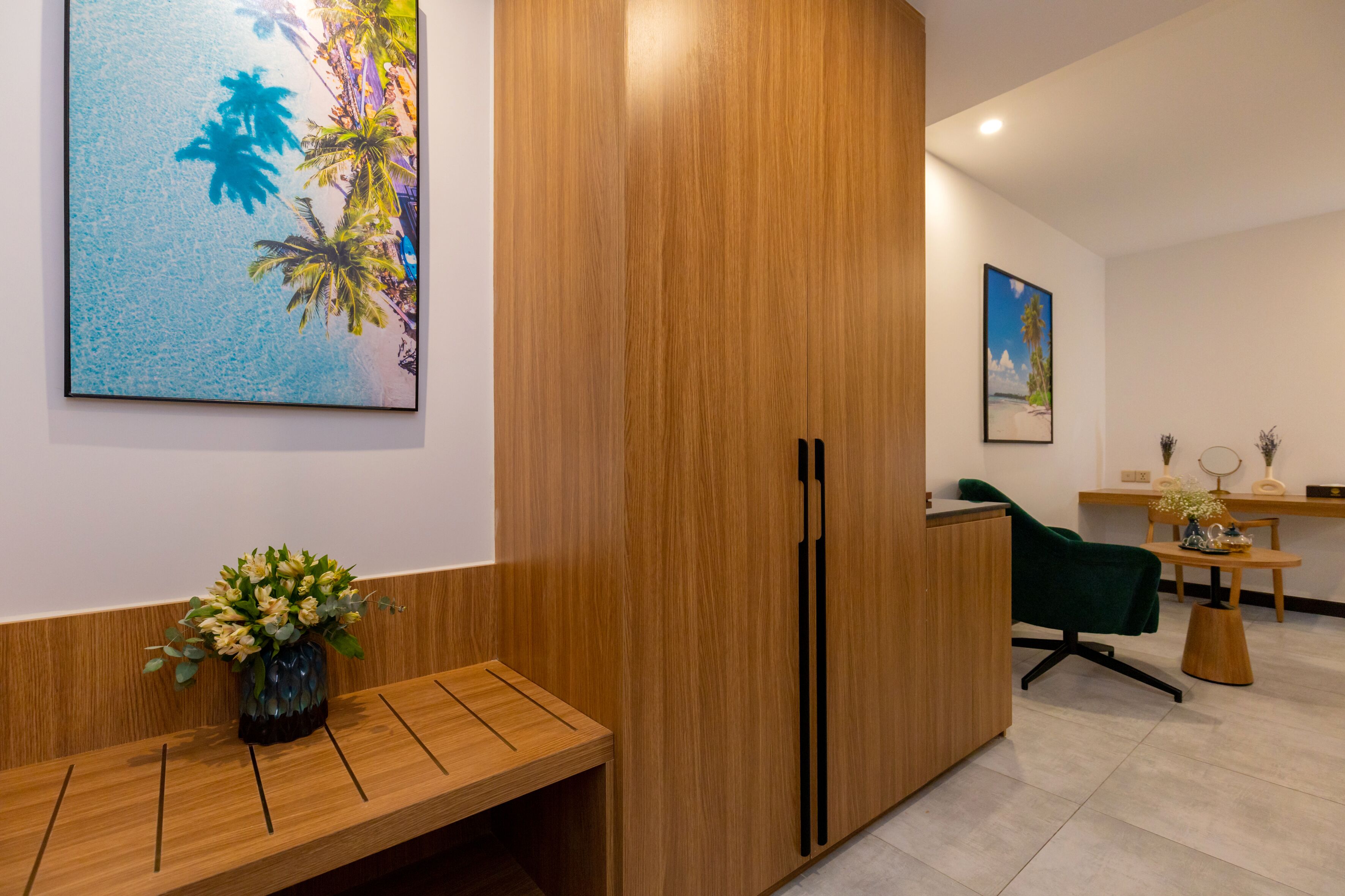 A reception area with a wooden reception desk, a green chair, a wooden cabinet, and a wall-mounted painting of palm trees.