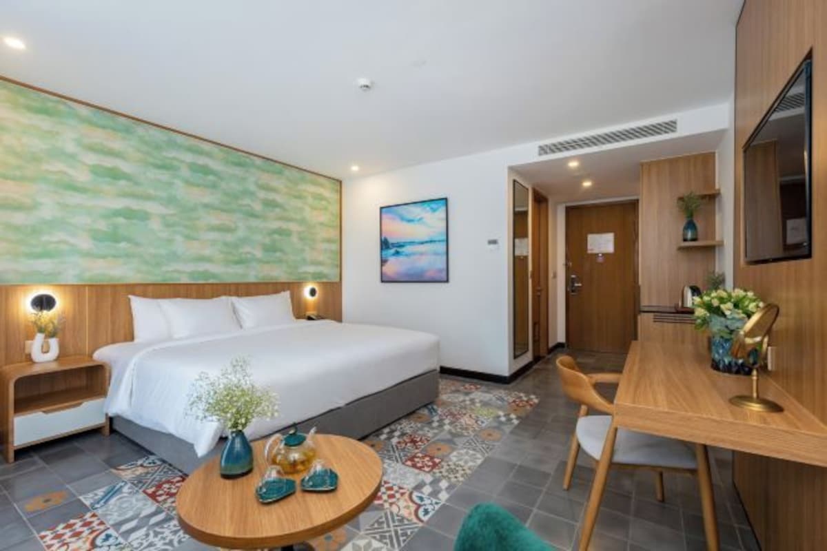 Habitación de hotel moderna con una cama grande, un escritorio y una silla. Hay un cuadro en la pared y un ventanal amplio.