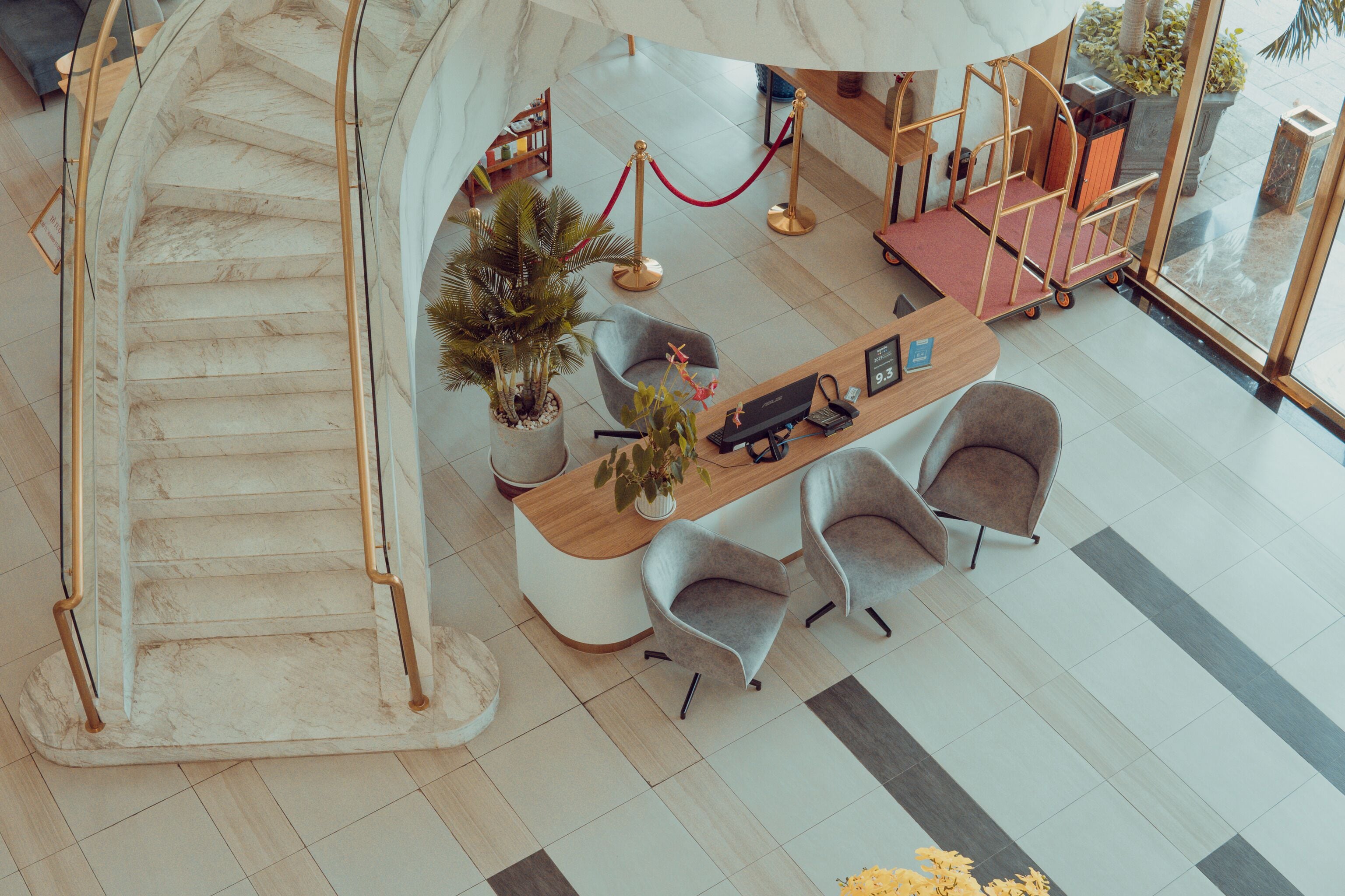 A hotel lobby with a marble staircase, reception desk, seating area, and a plant.