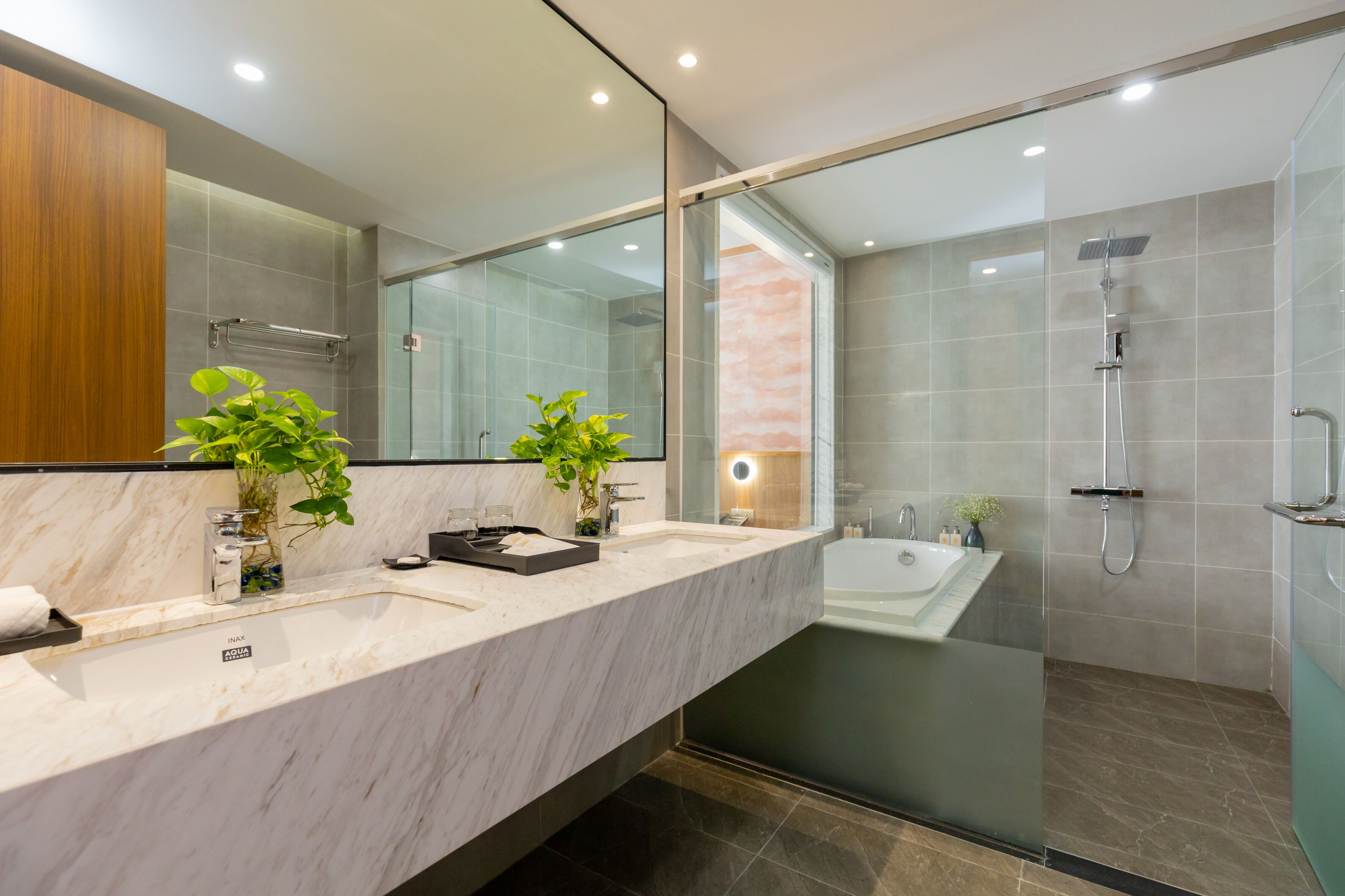 Un baño moderno con tocador de mármol, dos lavamanos, un espejo grande y cabina de ducha con paredes de vidrio.