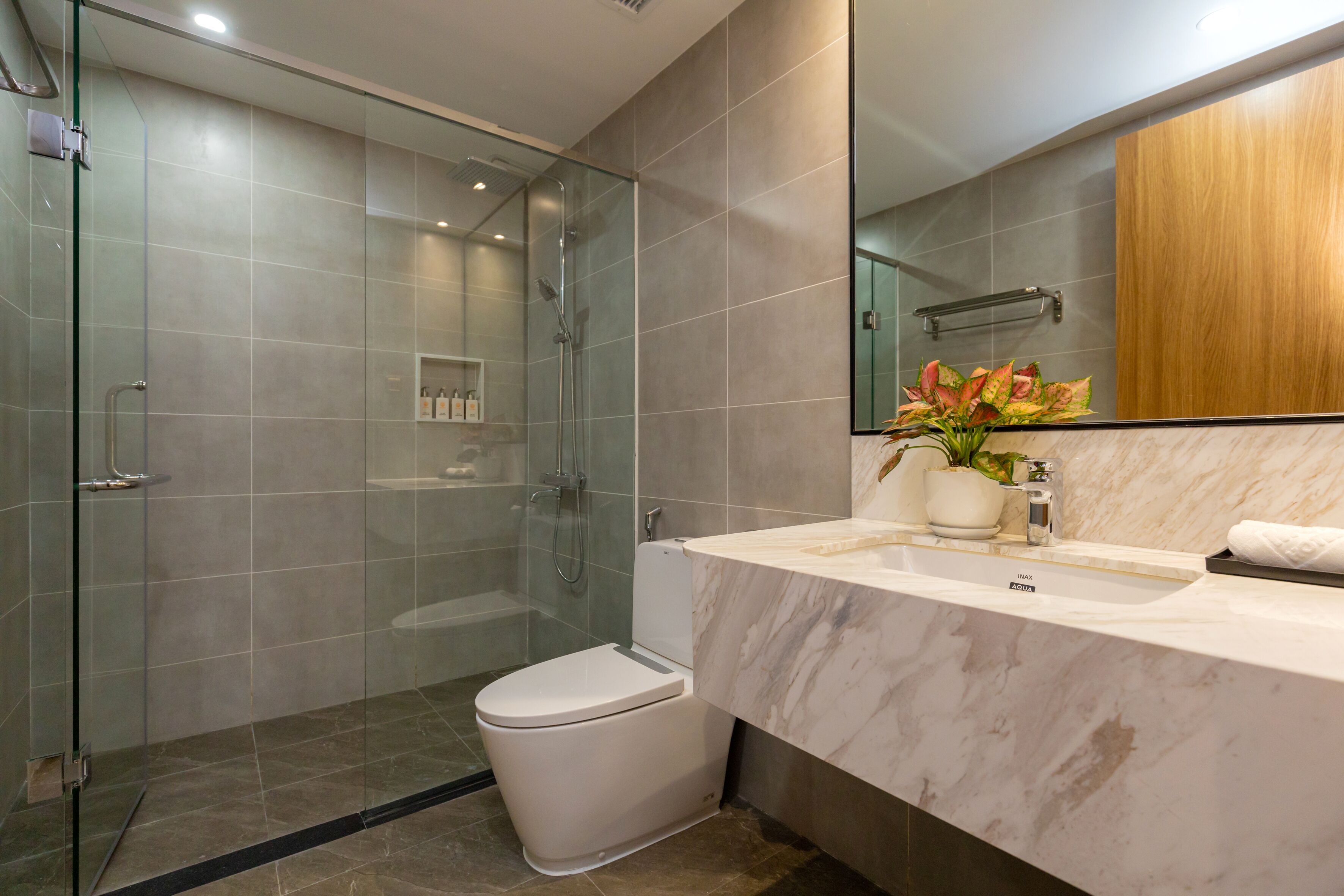 Een moderne badkamer met een douchecabine van glas, een wit toilet en een marmeren wastafel.