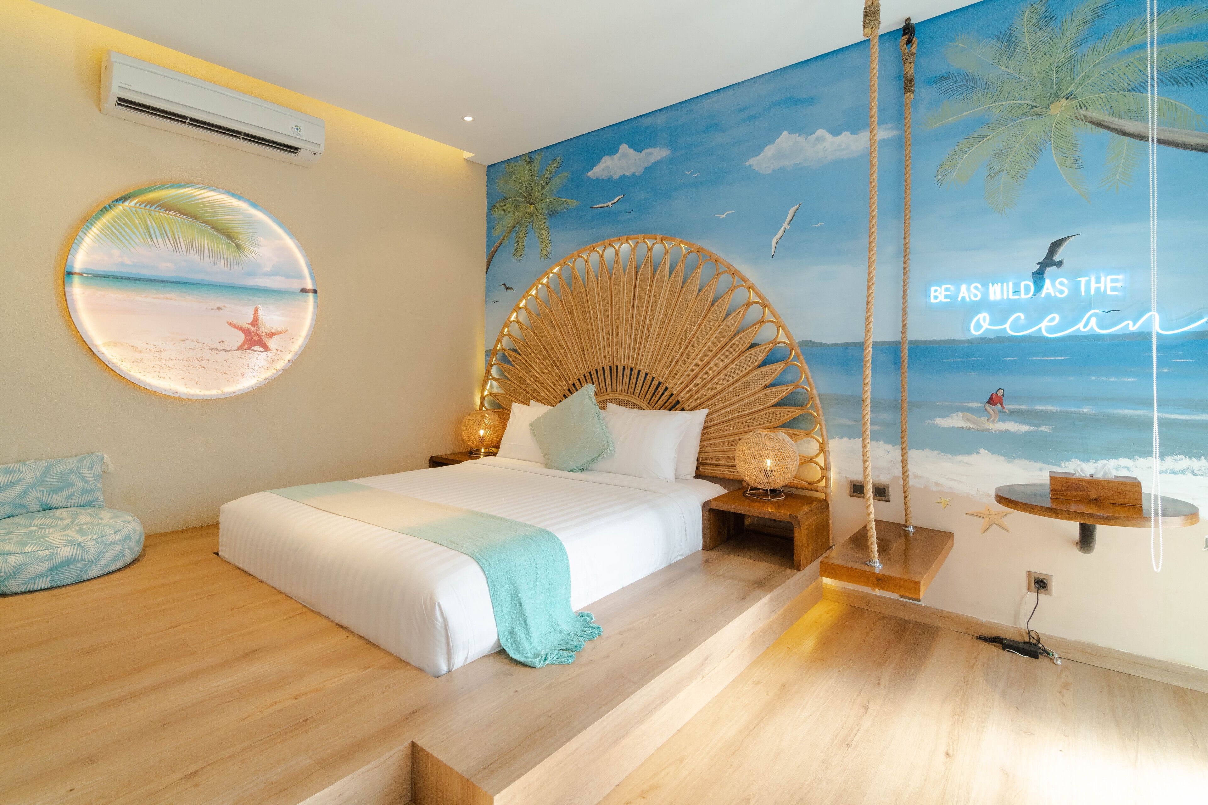 Quarto com um mural com tema praiano, um adorno redondo na parede e uma cadeira balanço.