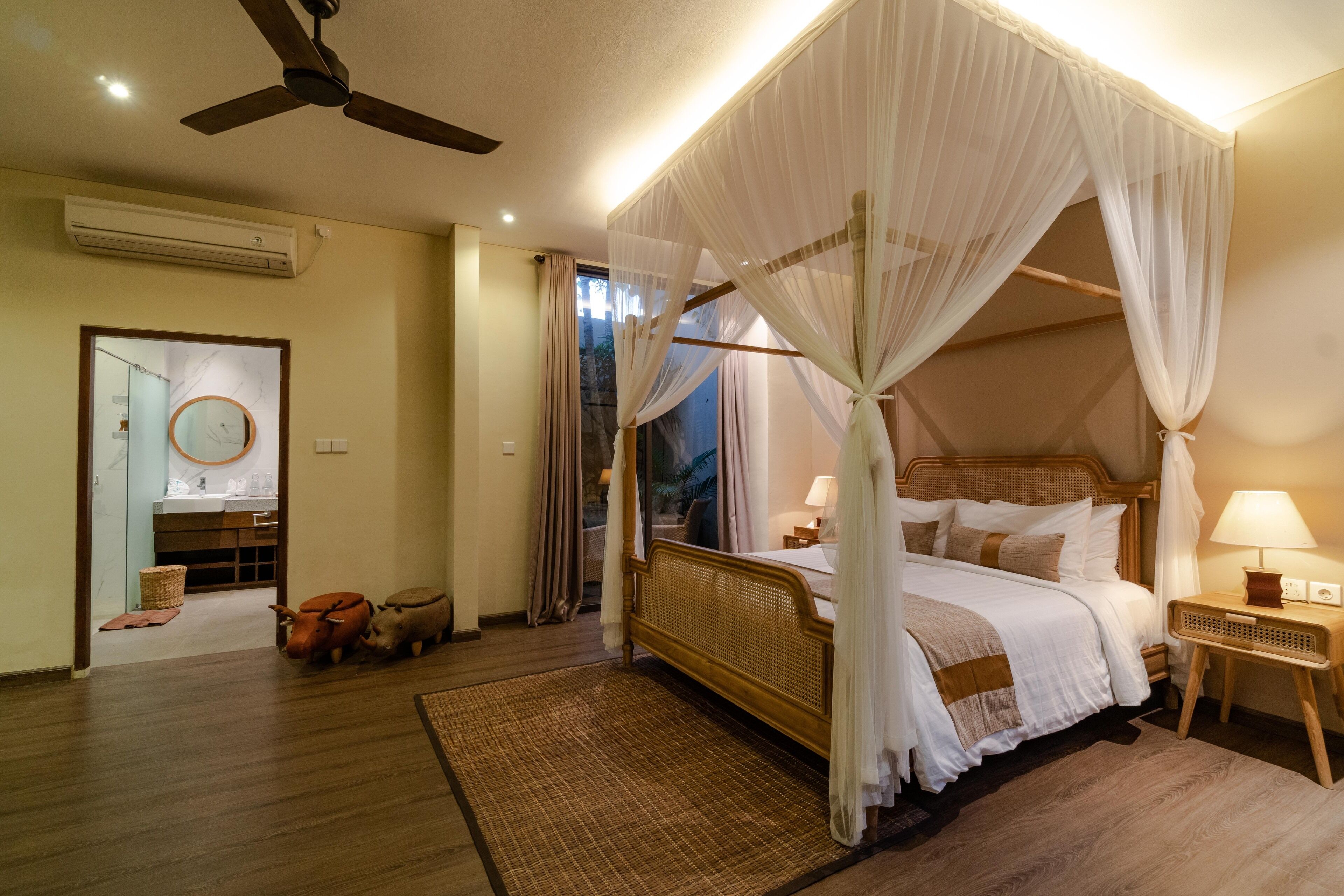 Une chambre à coucher avec un lit à baldaquin, un ventilateur de plafond, une table de chevet avec une lampe et une vue sur l’extérieur.