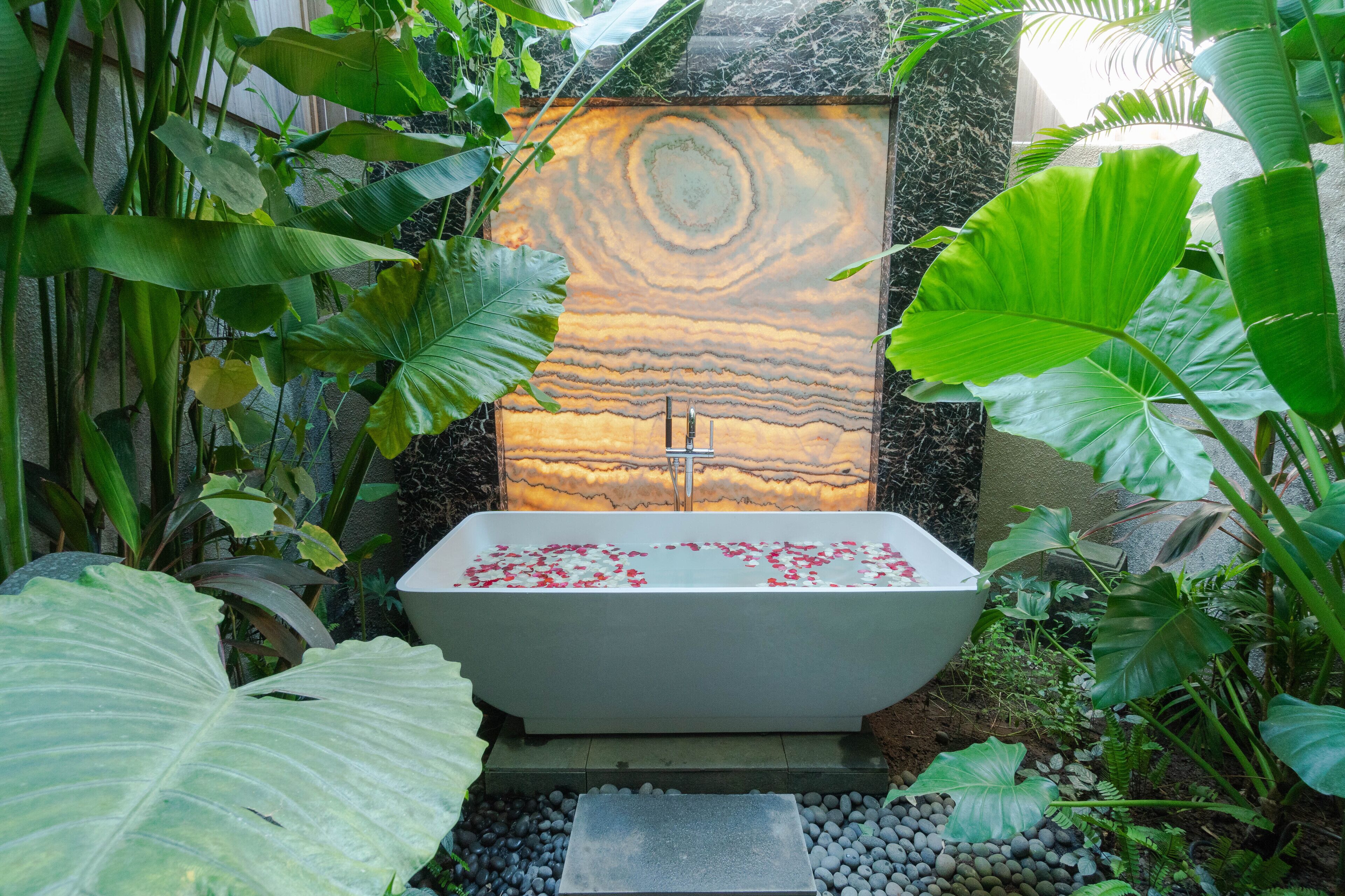 Une baignoire remplie de pétales de rose, entourée de plantes tropicales.