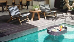 Un área de piscina con sillas de descanso, una mesa de comedor y una estatua.